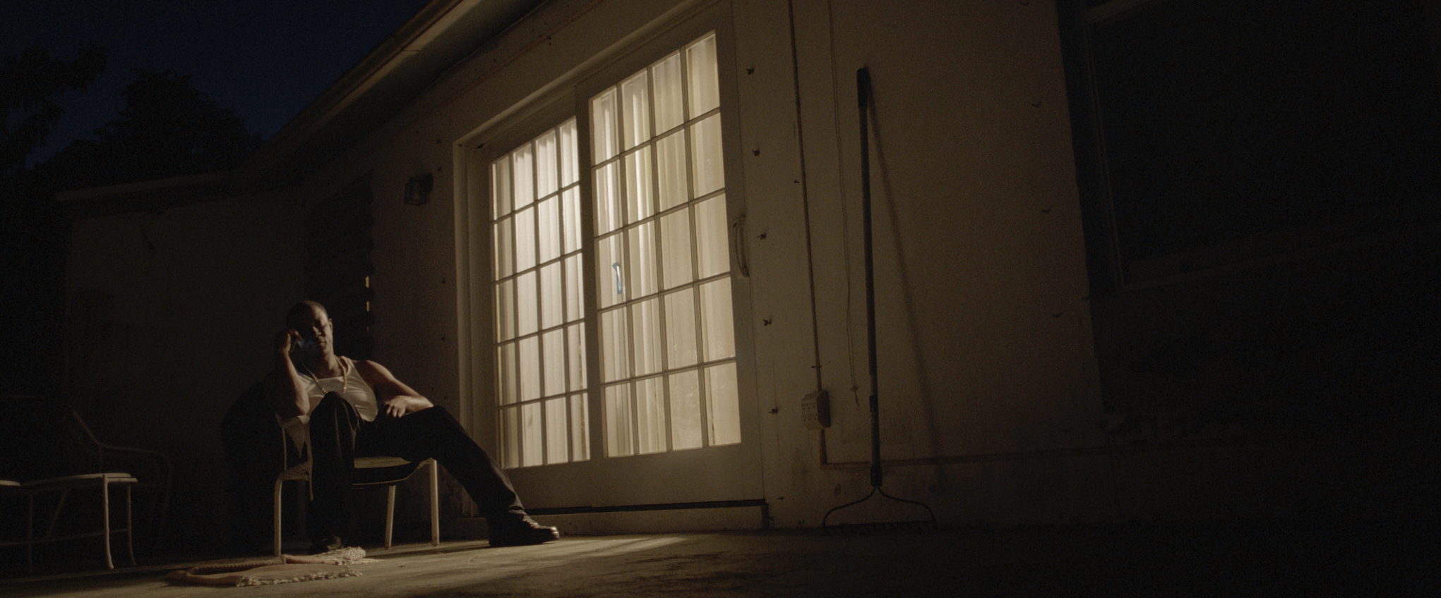 A figure sits alone in a dark room, lit only by the window behind them.