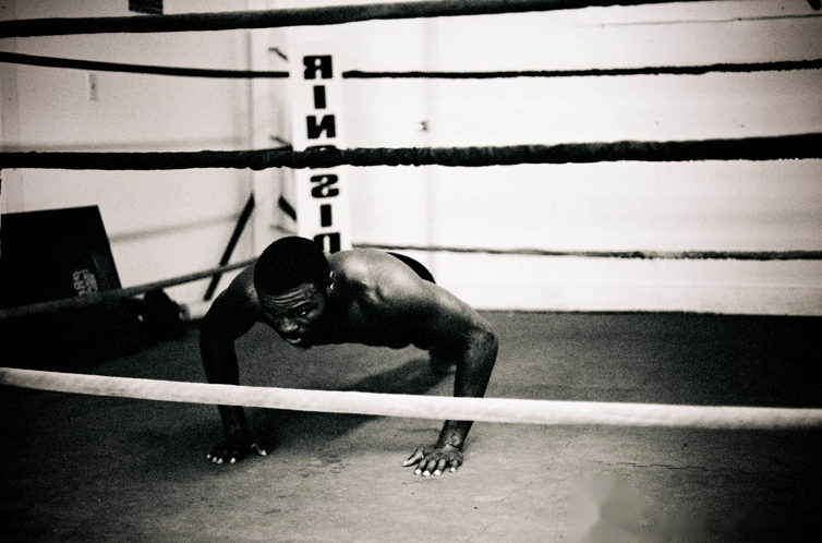 A boxer holds the bottom of a push-up on the floor of an empty ring.