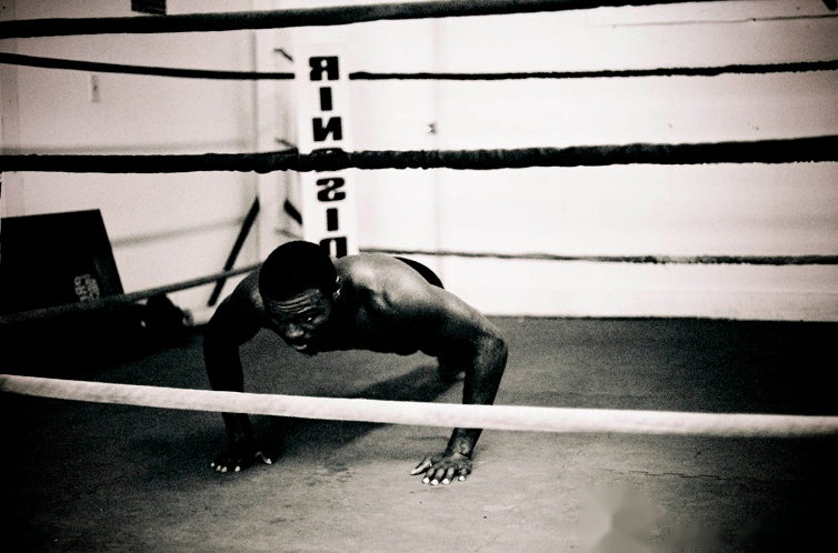 A boxer holds the bottom of a push-up on the floor of an empty ring.
