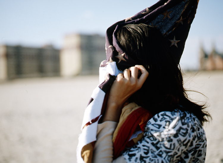 A woman draws the same flag around her face, holding it closed with one hand.